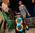 Woman dancing next to a JBL speaker at night with cityscape in the background